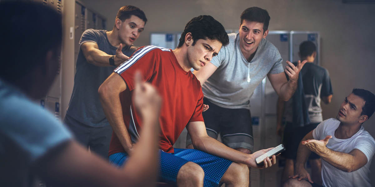 更衣室にいる10代の男子がスマホを持っている。ほかの男子からセックスをするよう強く勧められている。