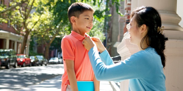 幼い息子のシャツのボタンをかけている母親