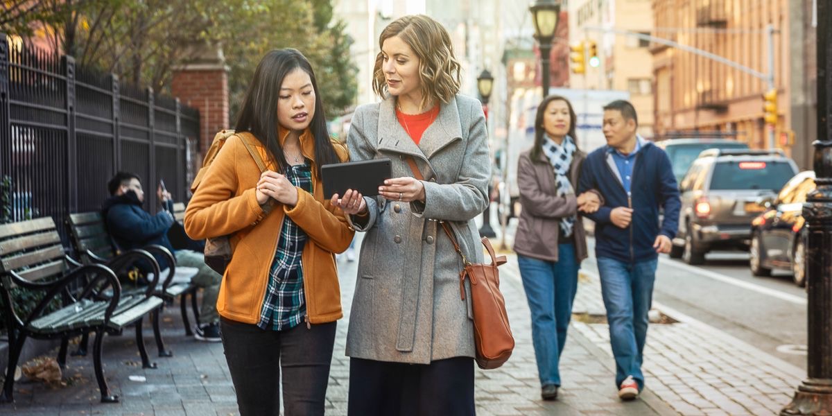 姉妹がアジア系の女性にタブレットを見せながら話している。