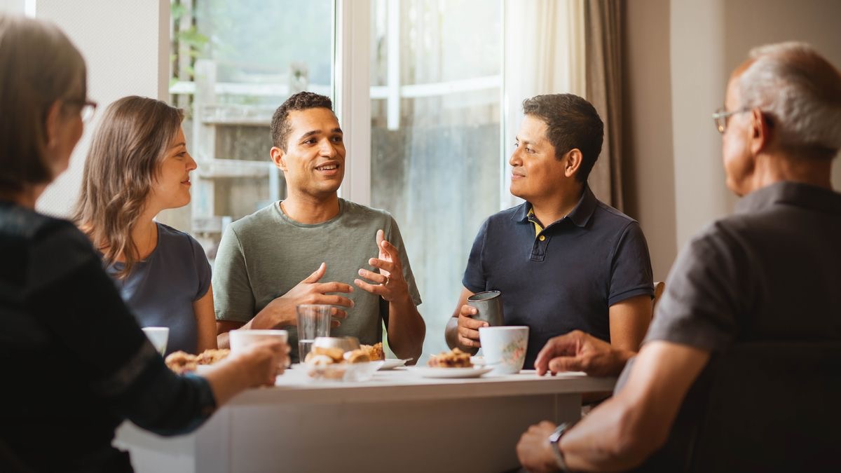 数人の兄弟姉妹が一緒に食事をしている。1人の兄弟が話しているのをほかの人たちがよく聞いている。