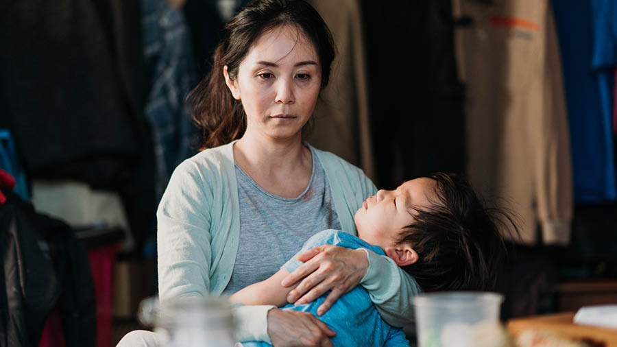 同じ女性がその日の終わりに，疲れ切った悲しげな顔で幼い息子を寝かし付けている。