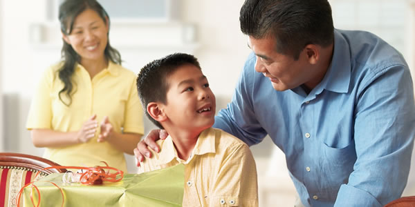 Parents talking to their young son as he unwraps a gift.