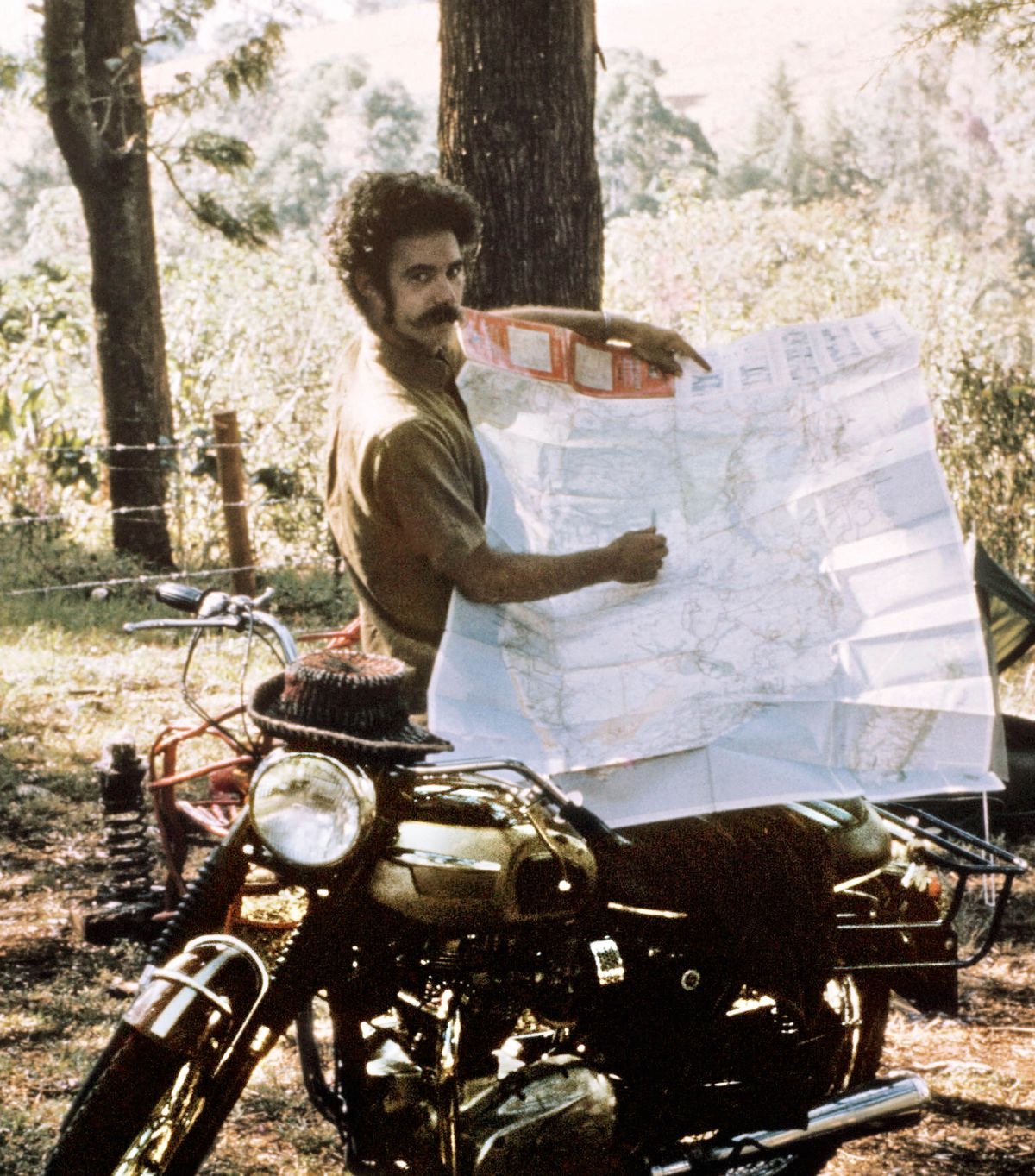 Robert li kêleka motorsikleta xwe sekinî ye û xerîteya rêwîtiya xwe nîşan dide.