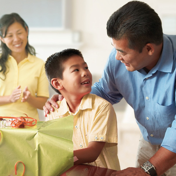 Parents smile as their little boy opens a gift