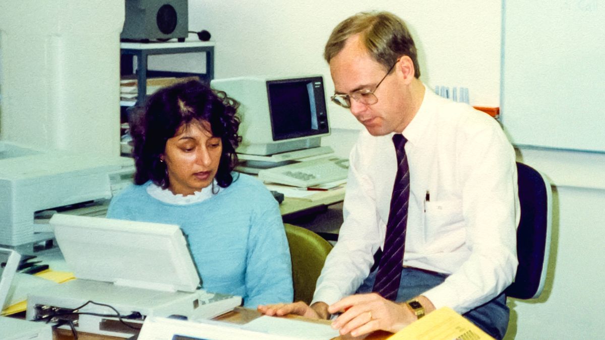 Kamal sentada delante de una computadora y recibiendo capacitación de un hermano.