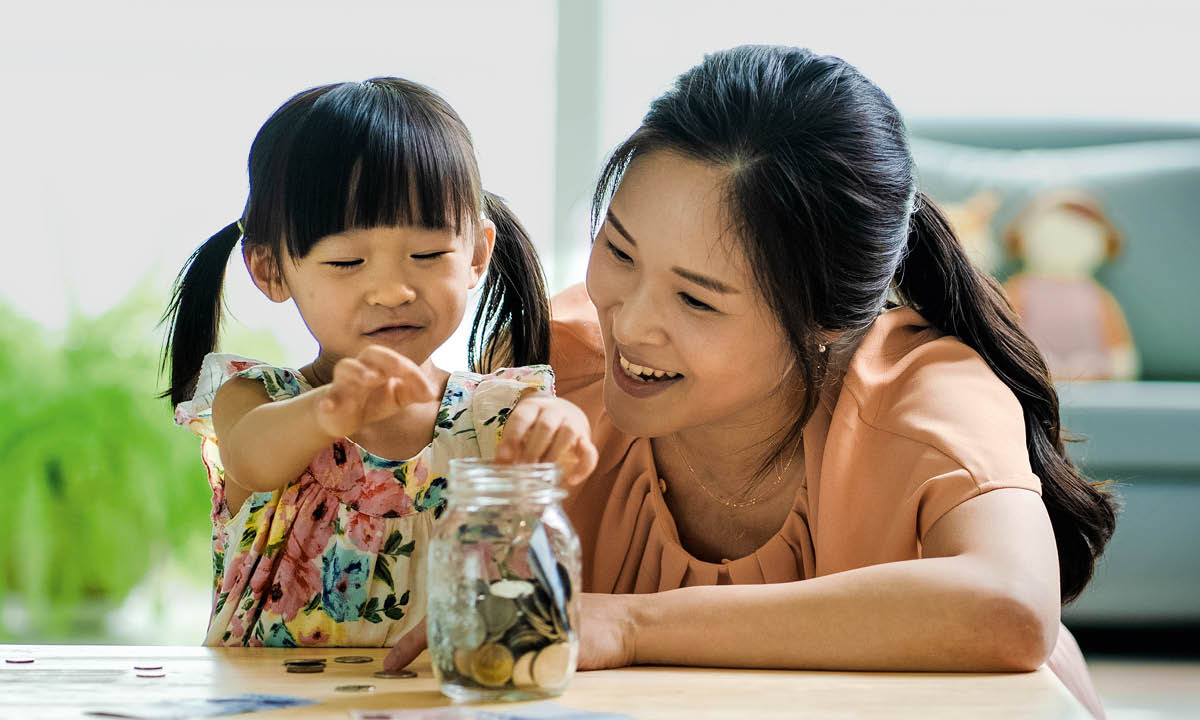 Seorang ibu membantu anak perempuannya memasukkan wang ke dalam balang kaca.