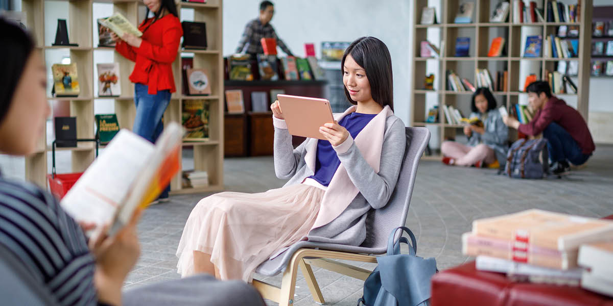 Seorang wanita di perpustakaan. Dia sedang membaca Bible dalam tabletnya.