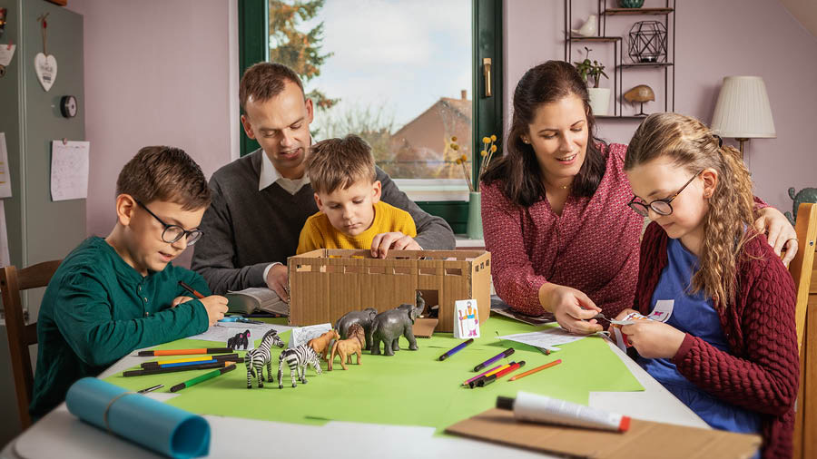 Pais com seus três filhos construindo uma maquete da arca de Noé com alguns animais.