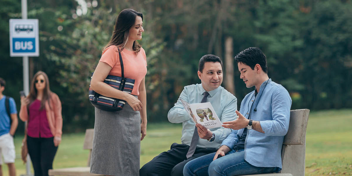 Een echtpaar gebruikt de ‘Voor eeuwig gelukkig!’-brochure bij een gesprek met een man bij een bushalte.