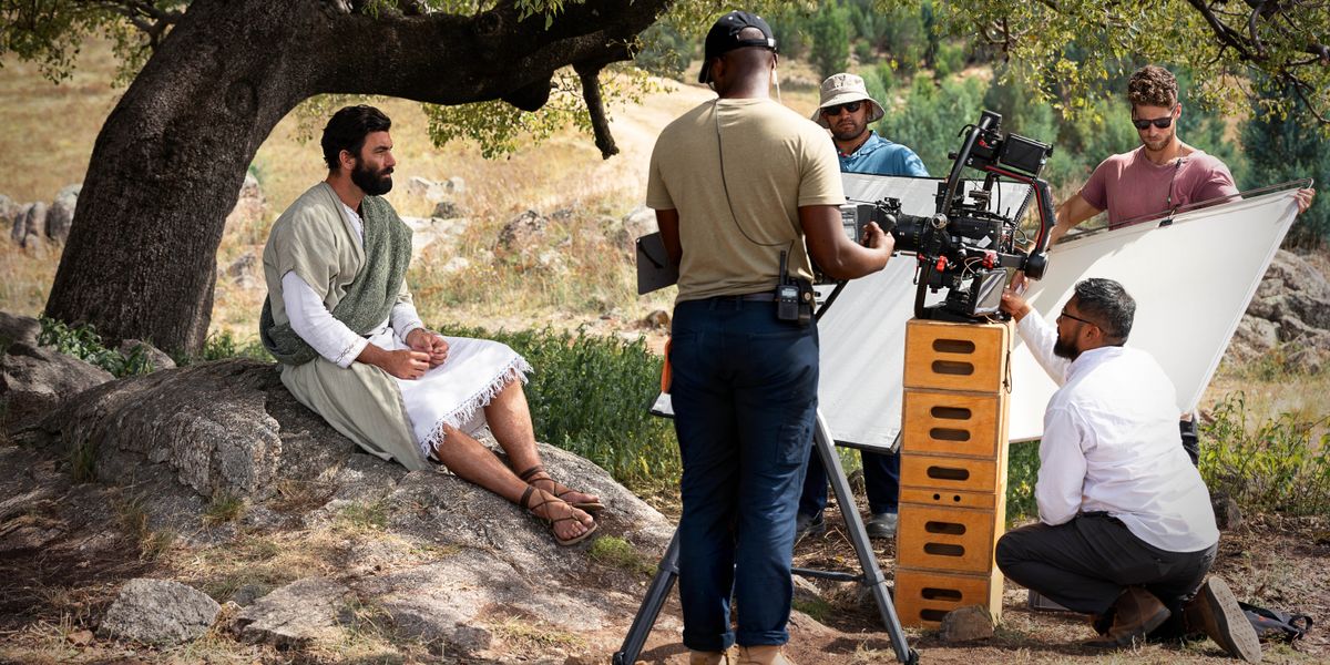 Et filmteam forbereder seg på å filme en utendørsscene i en episode av «Historien om Jesu liv og tjeneste». Han som spiller Jesus, sitter under et tre.