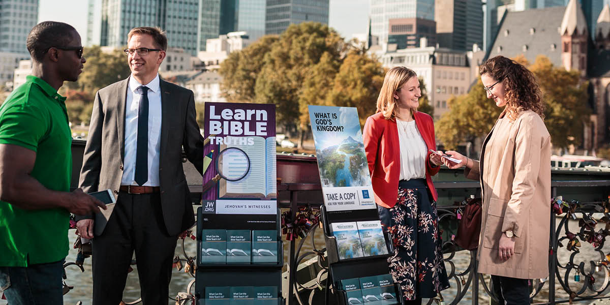En bror og en søster snakker med folk mens de står på stand. En av litteraturtrallene reklamerer for «Vakttårnet» nr. 2 2020.