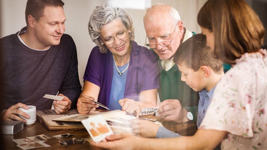 Et ektepar ser på bilder som vekker hyggelige minner fra deres liv i tjenesten for Jehova. Den voksne datteren deres og mannen og sønnen hennes er sammen med dem