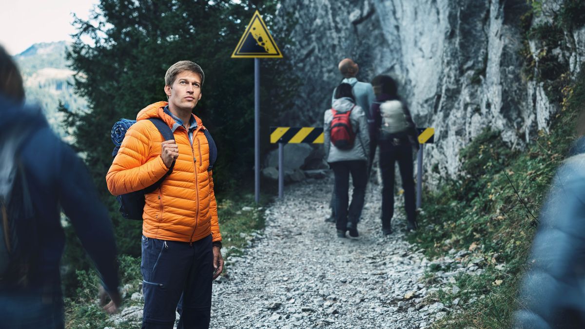 Den unge mannen står på en steinete sti som er merket med advarselsskilt. Andre turgåere ignorerer skiltene.