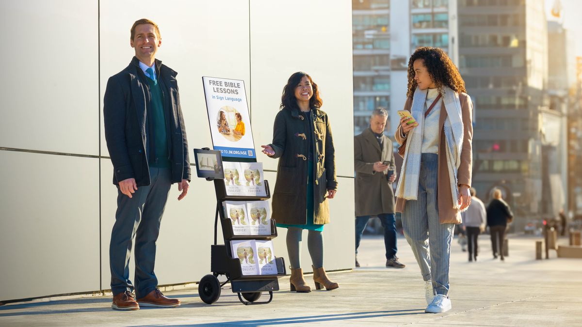 A couple at a witnessing cart advertising “Free Bible Course” as a woman walking by looks at the cart.