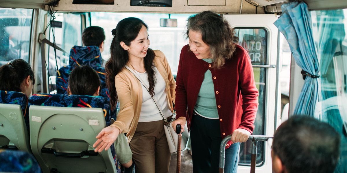 Un señora jong ta yuda un señora di edad pa yega na su luga di sinta den bus.