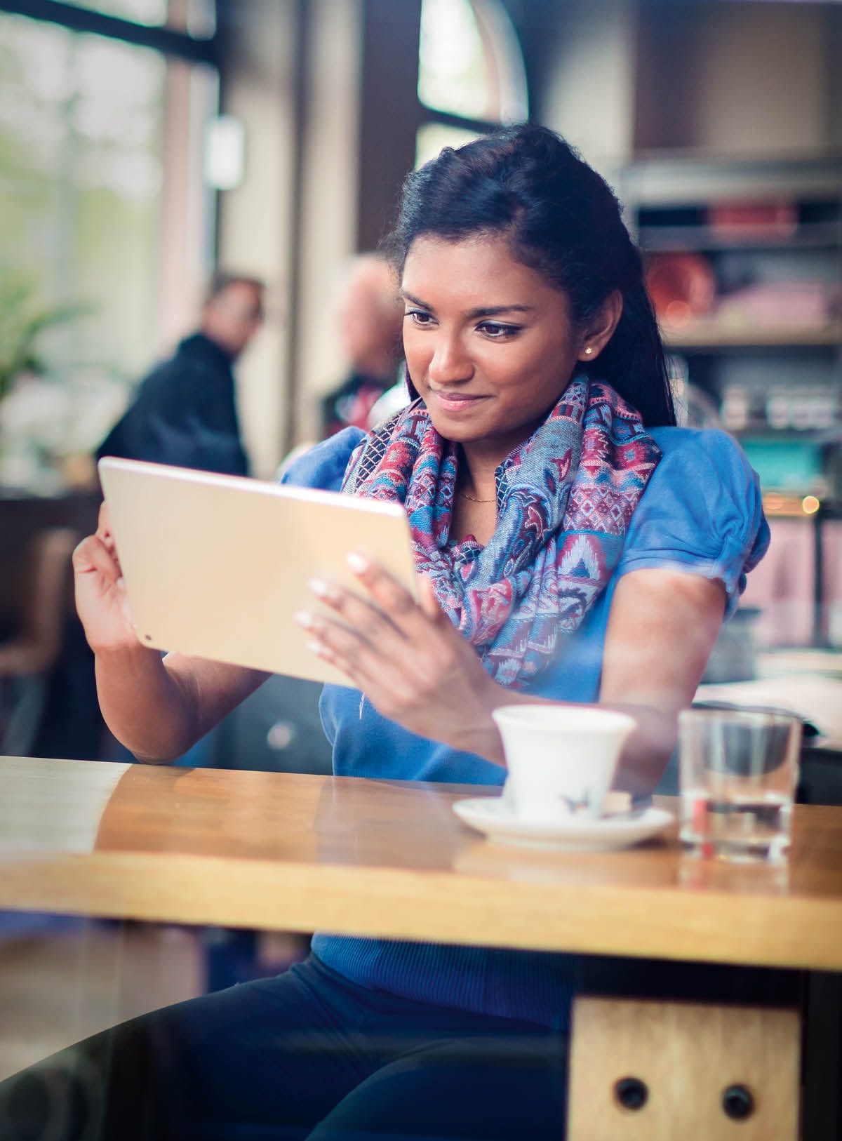 Un mucha muher hoben ta lesa Bijbel riba su aparato electronico den un café