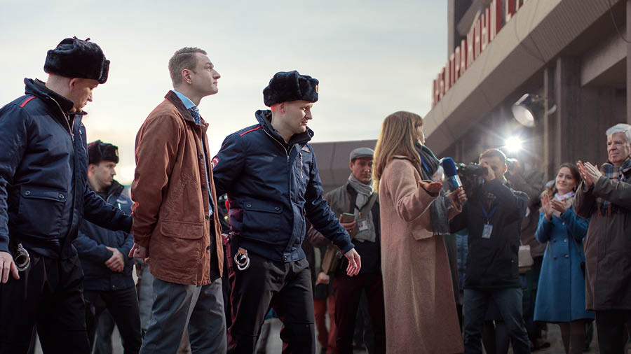 Policjanci prowadzą aresztowanego brata, czemu przyglądają się dziennikarze i jego współwyznawcy.