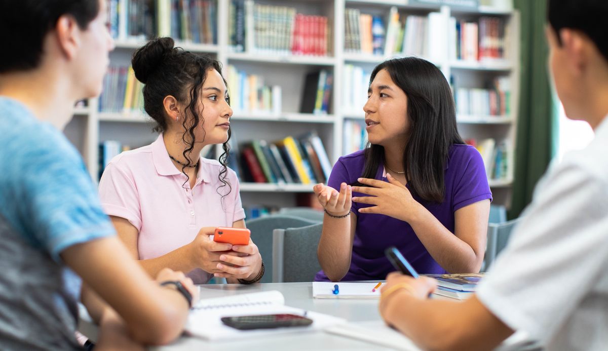 La misma joven hablando con sus compañeros de clase en la biblioteca de la escuela.