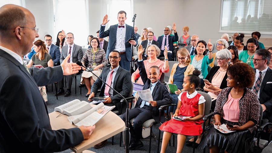 Brat prowadzi zborowe studium Strażnicy. Bracia i siostry podnoszą ręce, żeby dawać komentarze.