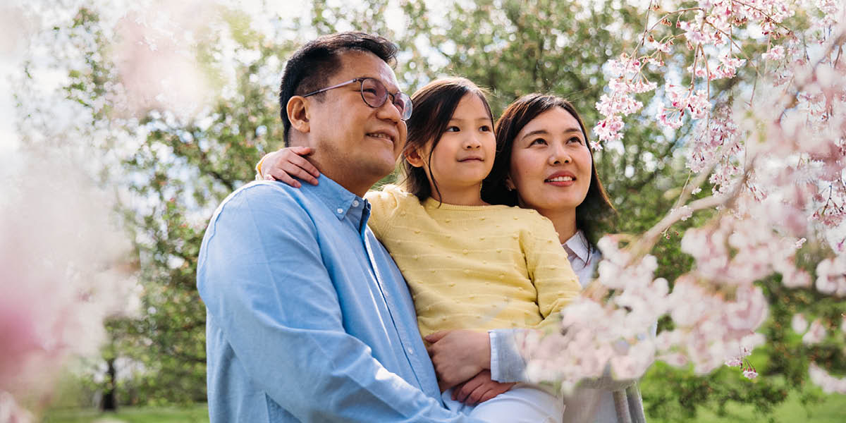 Rodzice ze swoją córeczką podziwiają kwiaty kwitnącej wiśni.