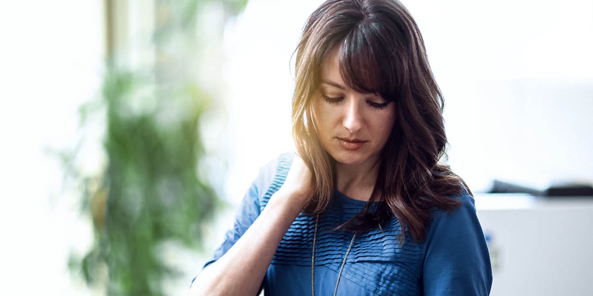 Uma mulher stressada no trabalho com a cabeça inclinada e um olhar muito triste.