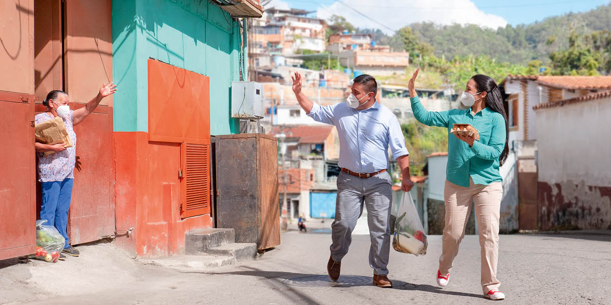 Um casal entrega alimentos a uma irmã idosa. Todos eles estão a usar máscara.