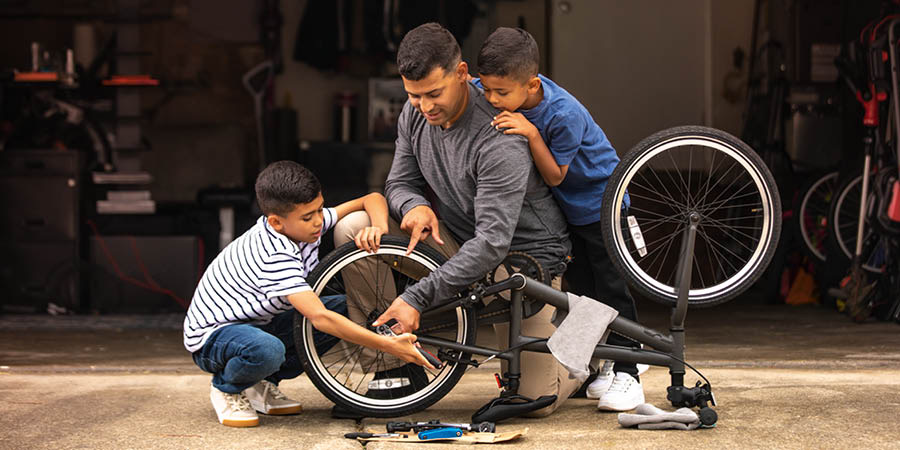 Um pai ensina os dois filhos a reparar uma bicicleta.