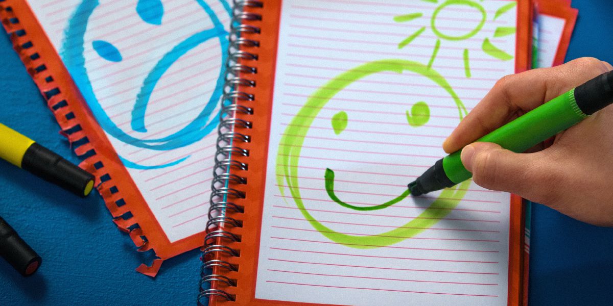 Um jovem faz um desenho de uma cara feliz e outra triste