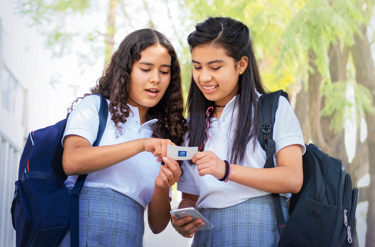 A mesma adolescente oferece um cartão do site jw.org a uma colega de escola.
