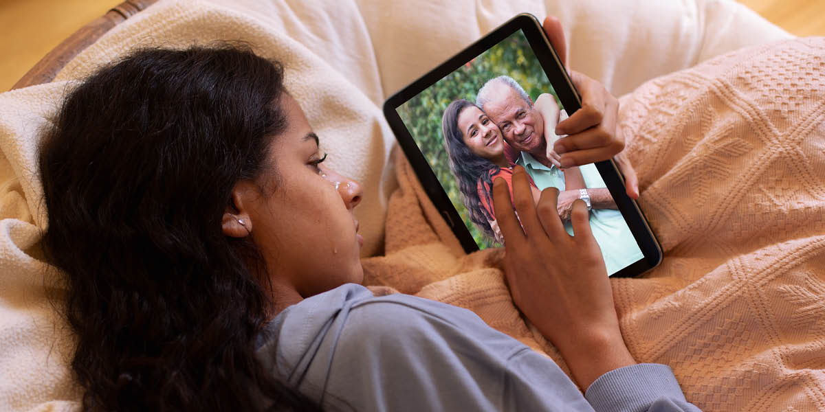 Uma adolescente deitada na cama a chorar. Ela está a olhar para uma fotografia dela e do avô juntos.