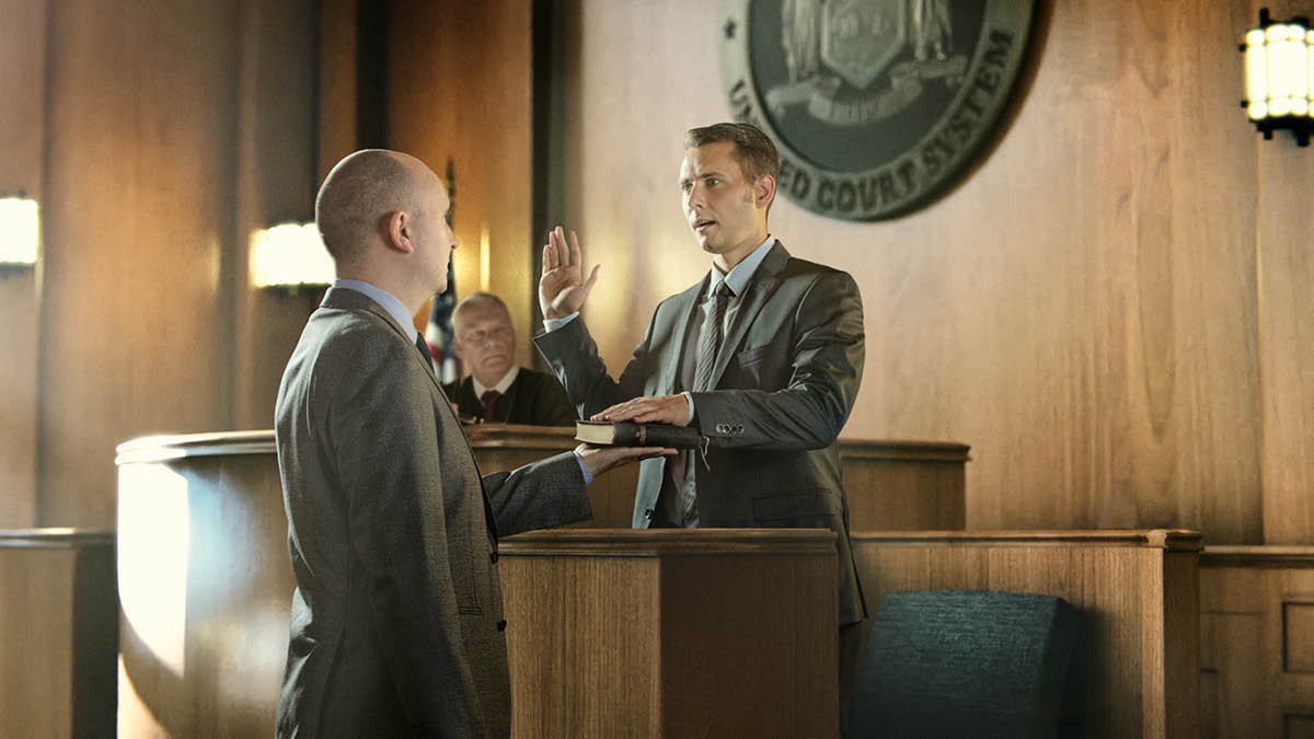 Um homem a fazer um juramento num tribunal. A sua mão direta está levantada e a esquerda está sobre a Bíblia.