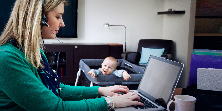 Uma mulher trabalha no computador enquanto seu bebê tenta chamar a sua atenção
