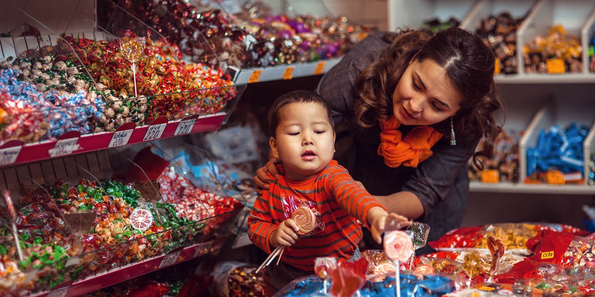 Uma mãe dizendo “não” ao filho, que está tentando pegar doces em uma loja