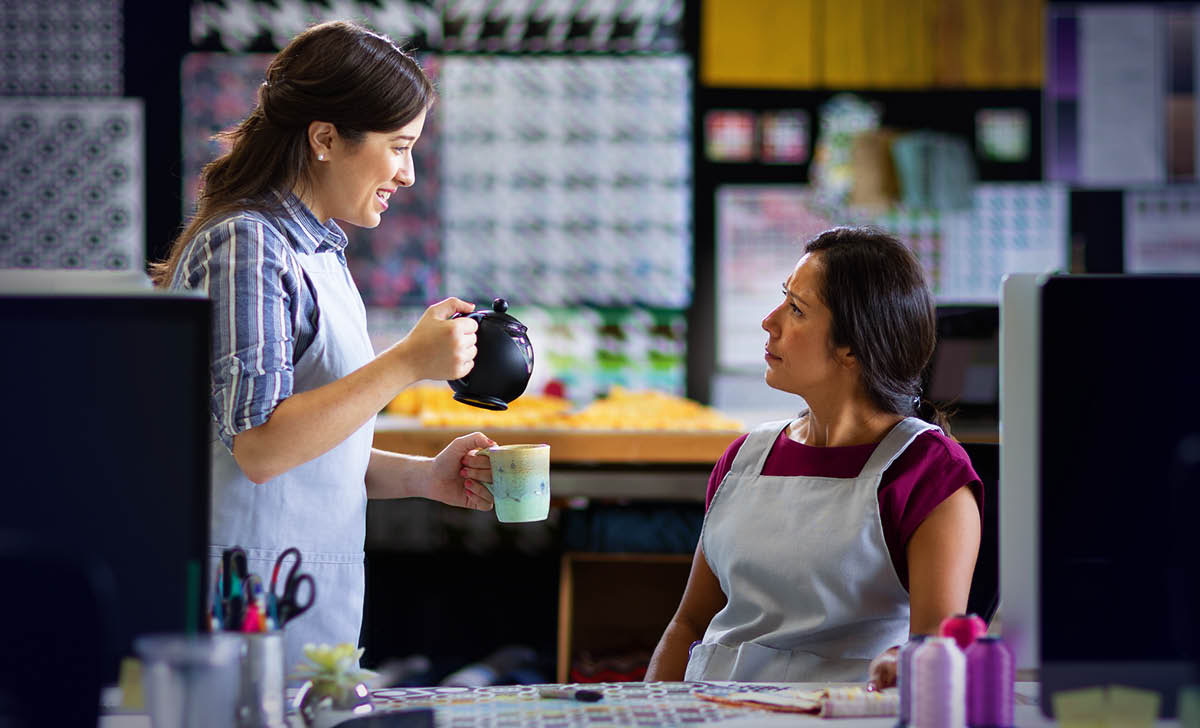 A mesma mulher sorri e oferece uma xícara de chá para sua companheira de trabalho, que fica surpresa.