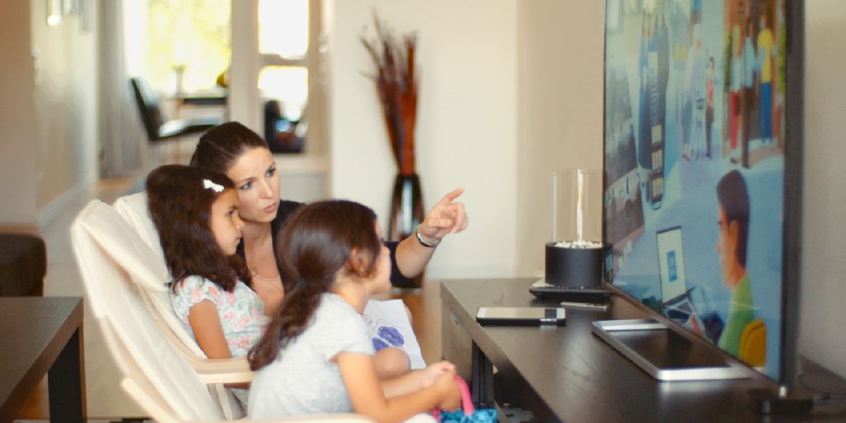 Talita está assistindo a um vídeo no site jw.org acompanhada da mãe e da irmã dela; a mãe de Talita descrevendo para ela o que está passando no vídeo