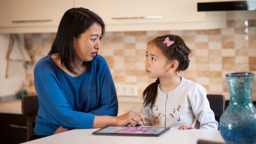 Uma mãe conversando com a filha sobre tomar cuidado com as diversões que ela vê no tablet