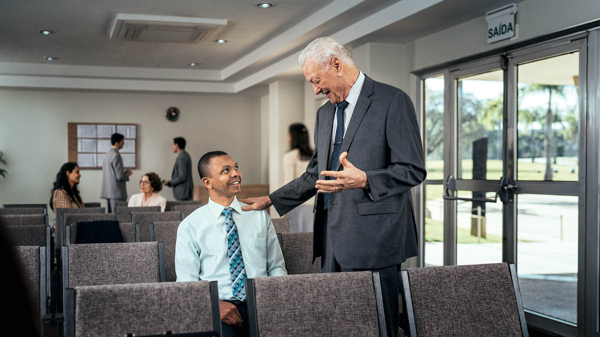 Um irmão idoso conversando de modo amoroso com um jovem sentado sozinho no Salão do Reino.