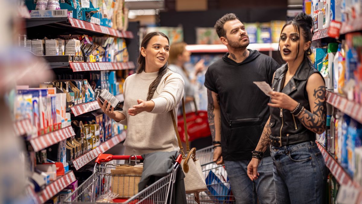Uma mulher ajudando um casal a encontrar um item no mercado. Ela trata o casal com bondade apesar de eles terem uma aparência bem radical e várias tatuagens.