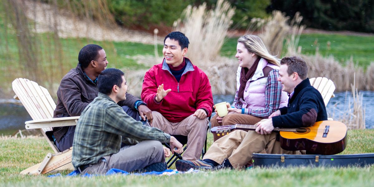 En un jardín, un grupo de jóvenes adultos hablando y pasando un buen rato.