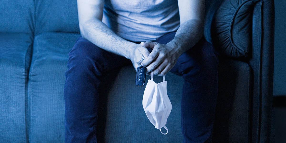 Un hombre sentado en un sofá, con las llaves del auto y una mascarilla en las manos.