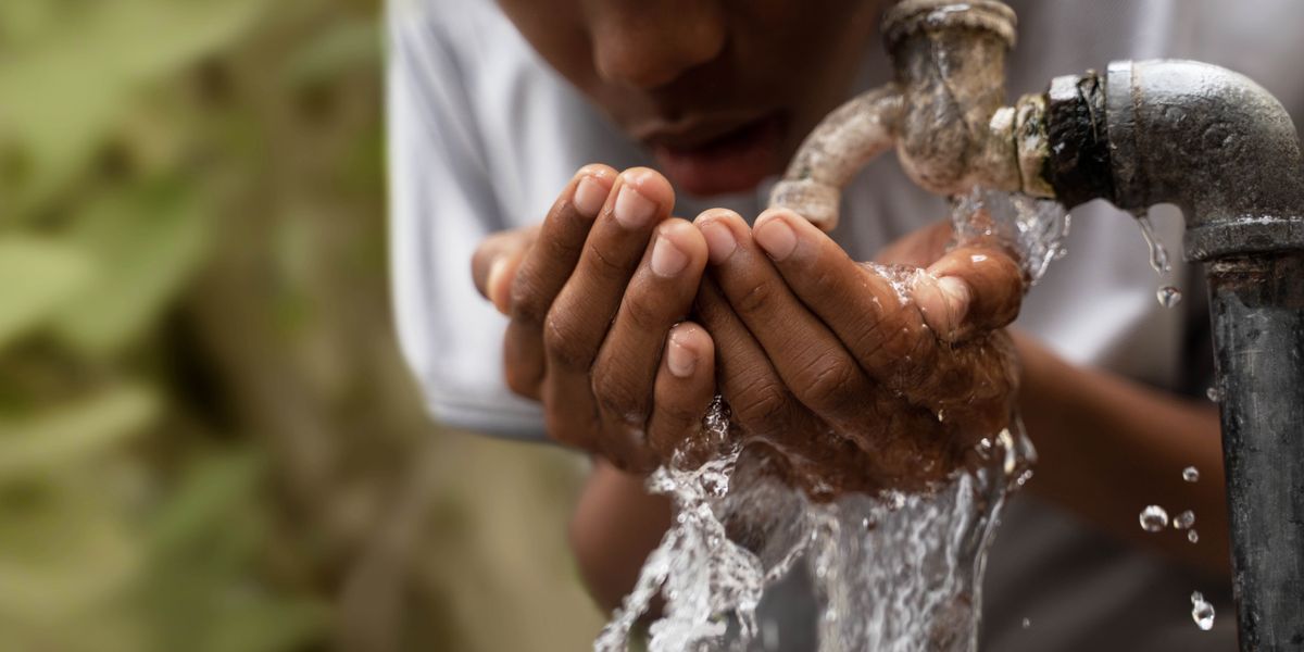 En la orilla de un río muy contaminado, un niño carga en la espalda a un niño más pequeño.