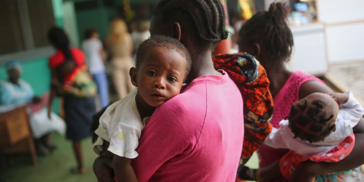 Un niño con lágrimas en los ojos en brazos de su madre. Esperan en una fila a que los atienda un médico.