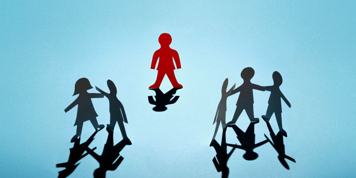 Un muñeco de papel está solo y separado de otros muñecos de papel que están juntos.