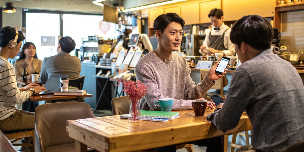 Akaari tetai tangata i roto i te café i tetai apinga ki tona oa i runga i tana smartphone.
