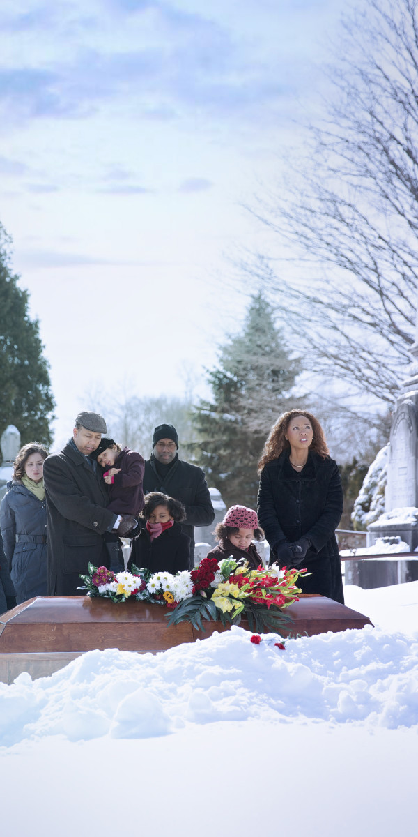 Adulţi şi copii stând în jurul unui sicriu la cimitir