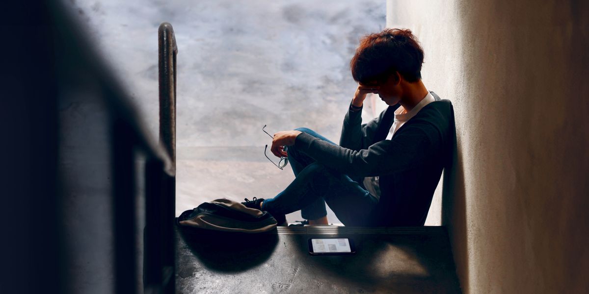 Подросток один сидит на ступеньках лестницы; кругом полумрак, и он удручённо склонил голову.