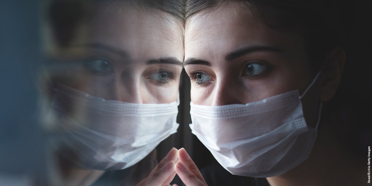 Женщина в маске смотрит в окно.