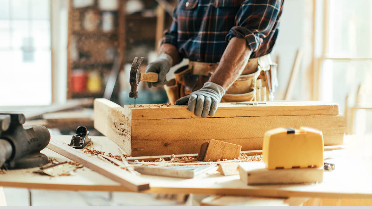 Um carpinteiro martelando um prego num pedaço de madeira.