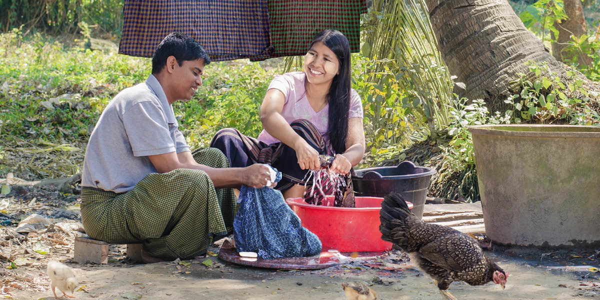 Um marido e uma esposa sorrindo enquanto lavam a roupa juntos.