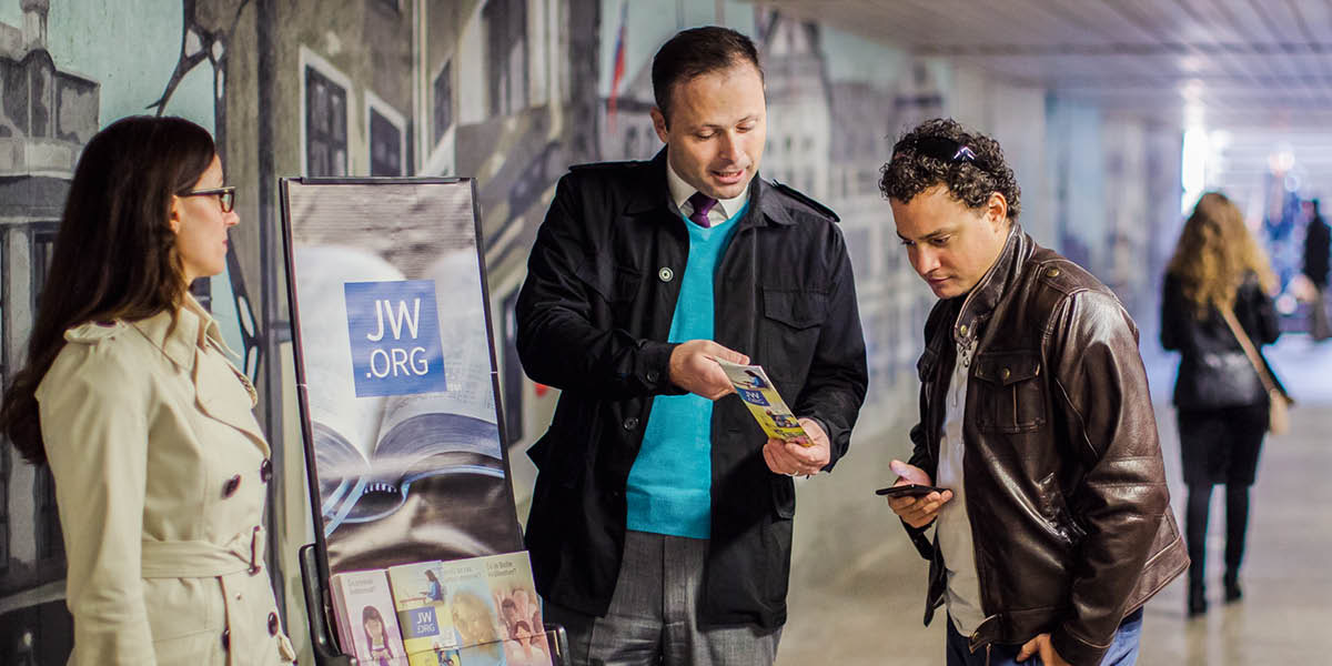Un couple qui prêche dans une station de métro à l’aide d’un présentoir mobile donne un tract à un homme.